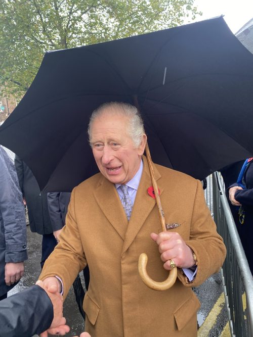 King Charles shakes hands with the public while holding an umbrella