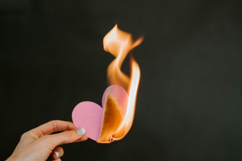 A pink paper heart is burning in front of a black background