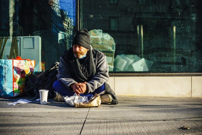 Homeless man sat amongst bags with a cup of coffee