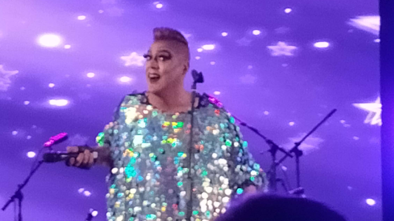 A drag act performs in a sequin dress, looking at the camera.