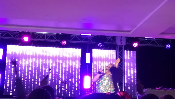 A drag queen performs on a purple stage.