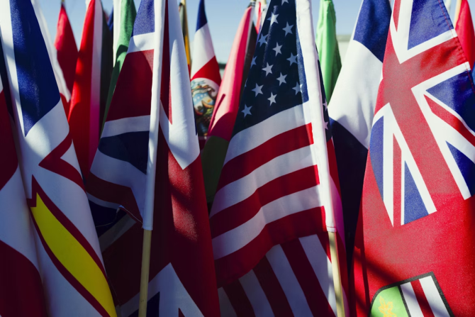 Display of Colorful National Flags on Sticks in the Daytime - A close-up shot of a collection of various national flags on wooden sticks, displayed outdoors in the daytime. The flags are arranged in a cluster, with the American flag and the British flag prominently featured. Other flags are visible in the background, but their details are obscured.